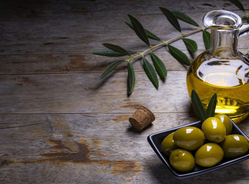 Tasty looking olives extra virgin olive oil and olive leafs on dark wooden background